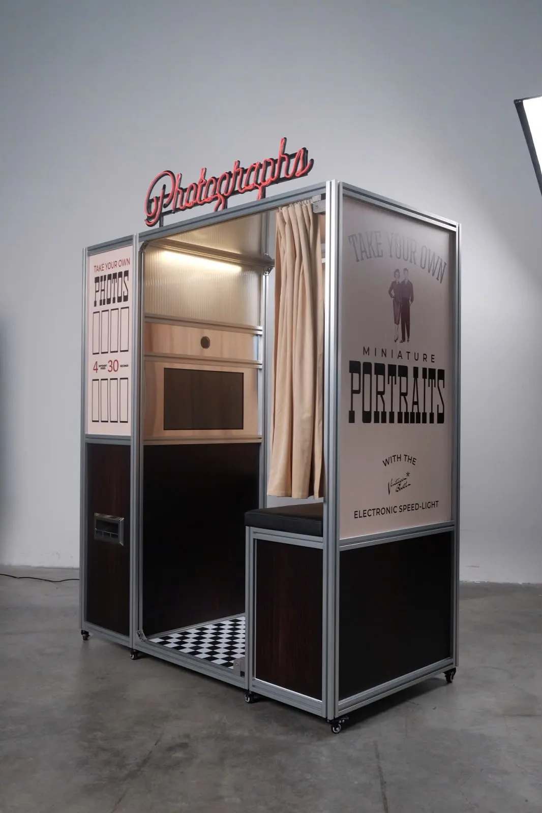Inside the enclosed photo booth: the camera, warm interior light, bench, and checkerboard floor