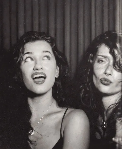 Film photo booth strip frame four: one friend laughing up at the ceiling, the other pouting, the keeper