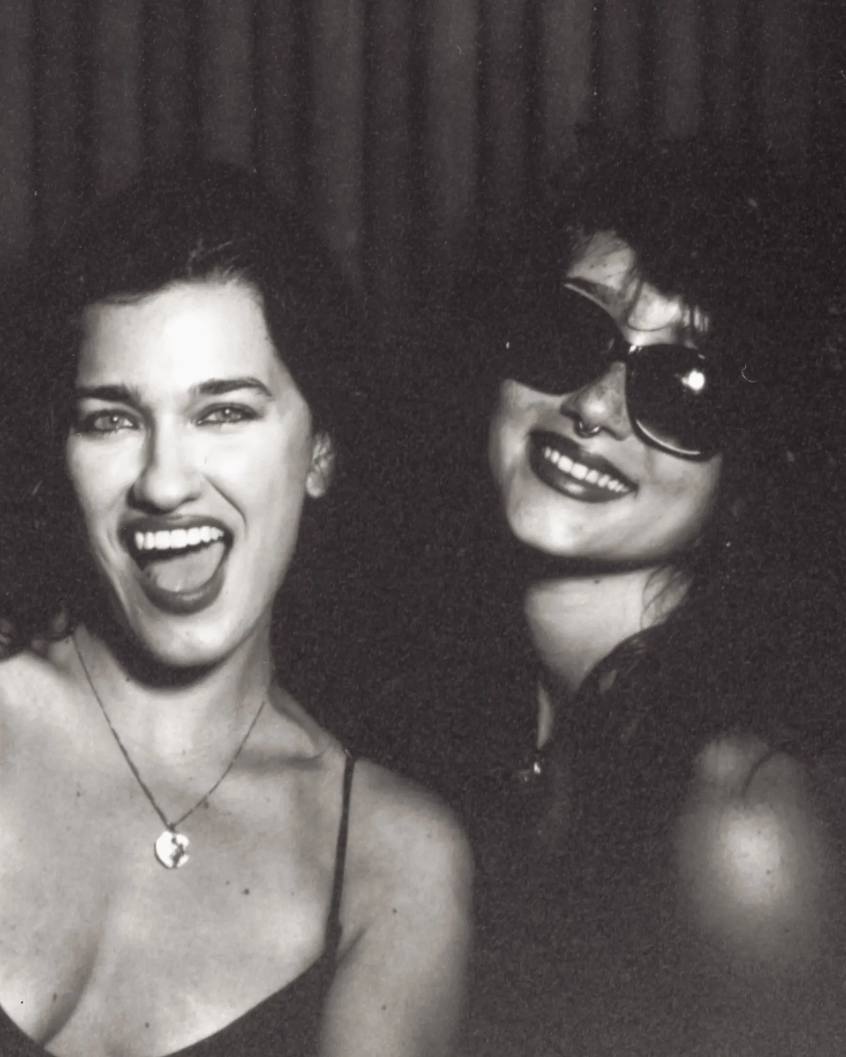 Black and white photo booth print: two friends mid-laugh, one in sunglasses